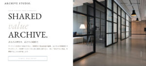 ARCHIVE STUDIOのオフィス内部。黒いフレームの大型ガラスパーティションで仕切られたモダンな空間。奥に白いランプスタンドと家具が見える。床はコンクリート調で天井には黒いペンダントライトが配置されている