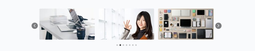 ビジネスオフィス環境を3枚の写真で構成するスライダー。左画像はデスクの上にノートパソコンと書類が置かれたオフィス風景、中央画像はオレンジ色のジャケットを着た女性が手を上げている人物写真、右画像はデスク上に整理整頓された文房具や電子機器のフラットレイ。下部にスライドナビゲーションドット、左右に移動矢印がある