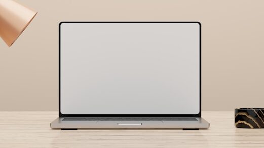木製デスクの上に開いたノートパソコンが置かれ、左上に銅色の植木鉢、右側に装飾品が配置されたミニマルなワークスペース。